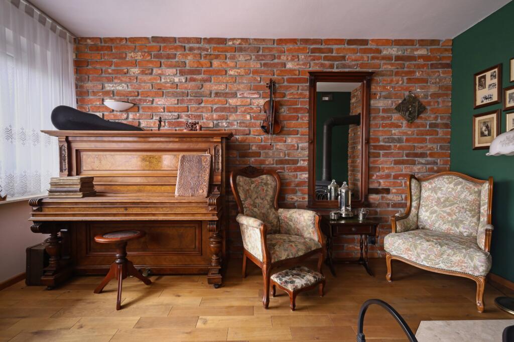Salon w stylu retro z pianinem, fotelem stylizowanym na styl angielski, piękną czerwoną cegłą oraz zielonymi ścianami