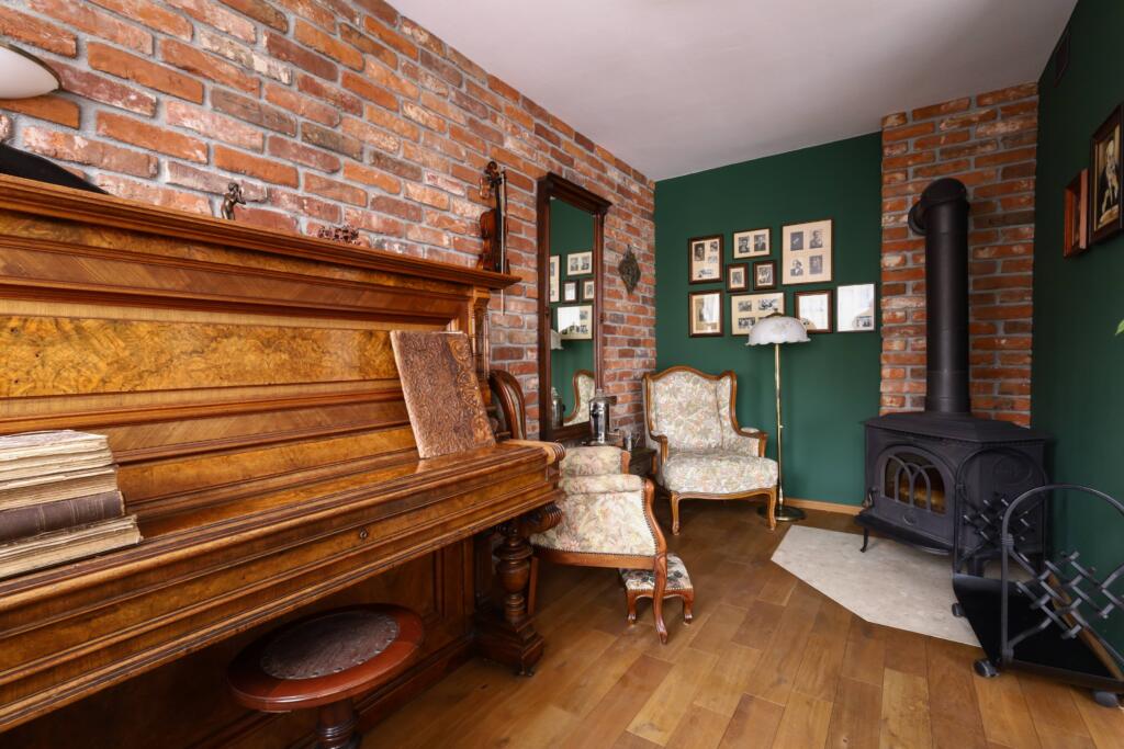 Retro salon w stylu angielskim z czerwoną starą cegłą na ścianie oraz stylizowanymi fotelami i pianinem