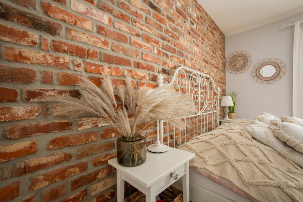 Sypialnia z białym łóżkiem oraz ceglaną ścianą w stylu glamour