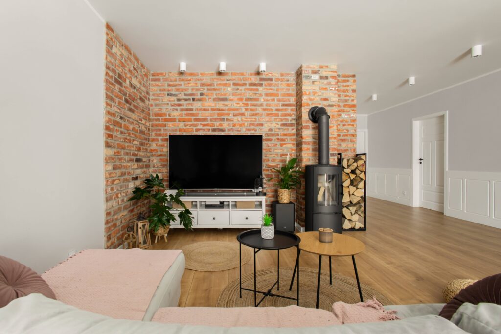 Salon z kominkiem oraz ceglaną ścianą z drewnianą podłogą oraz dużym narożnikiem