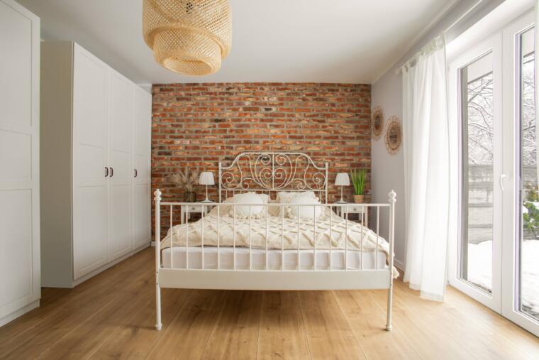 Sypialnia w stylu glamour z białym łóżkiem, białymi meblami i ścianą z cegły