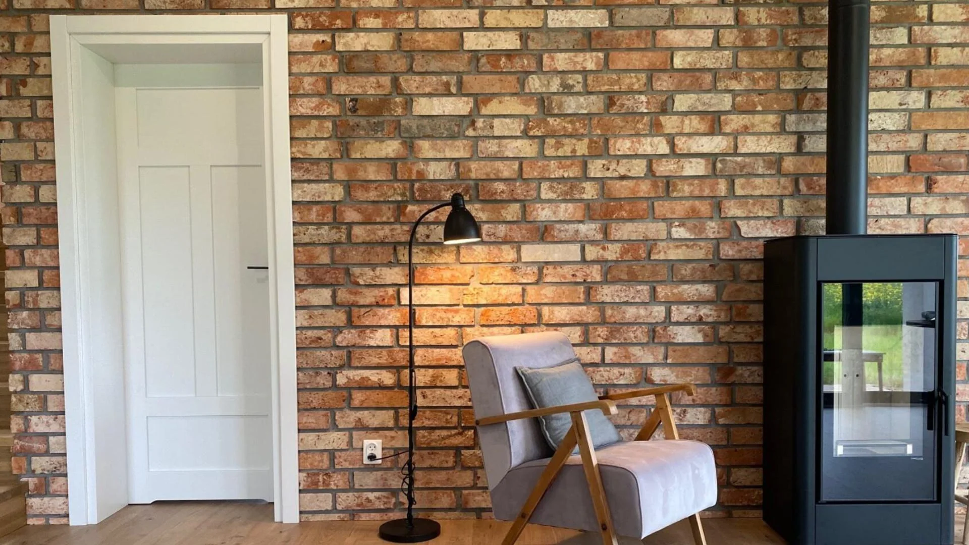 Salon z ceglaną ścianą, kominkiem i stylowym fotelem w klasycznym wnętrzu.